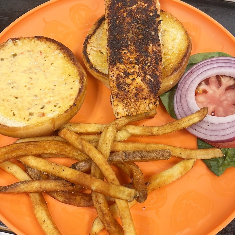 Lutfi’s Raymore seafood sandwich with a toasted bun, grilled fish, lettuce, tomato, onion, and fries.