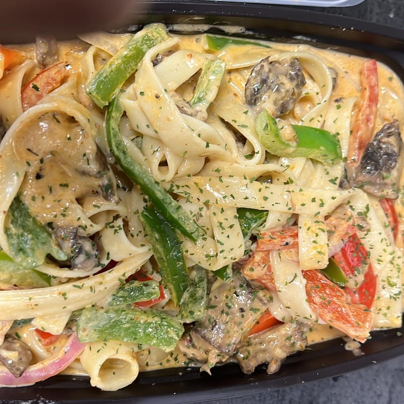 Creamy seafood pasta with bell peppers, onions, and mushrooms in a black container.